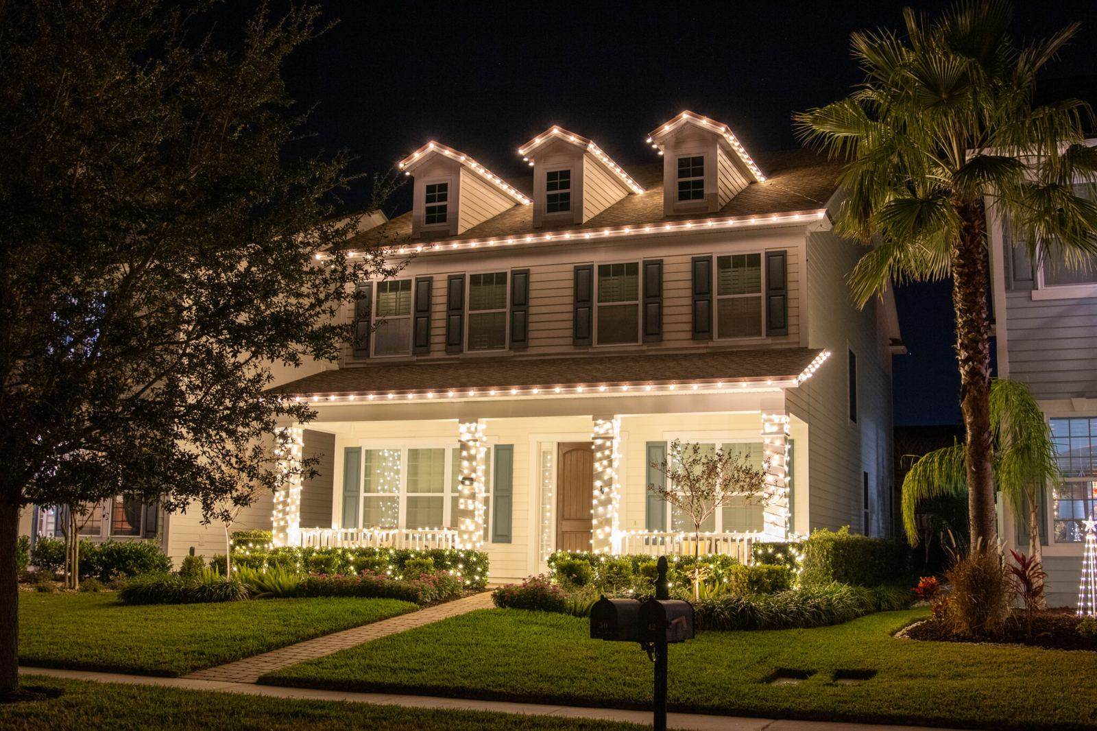 Warm white lighting outlining a home's dormers, roofline and columns at night