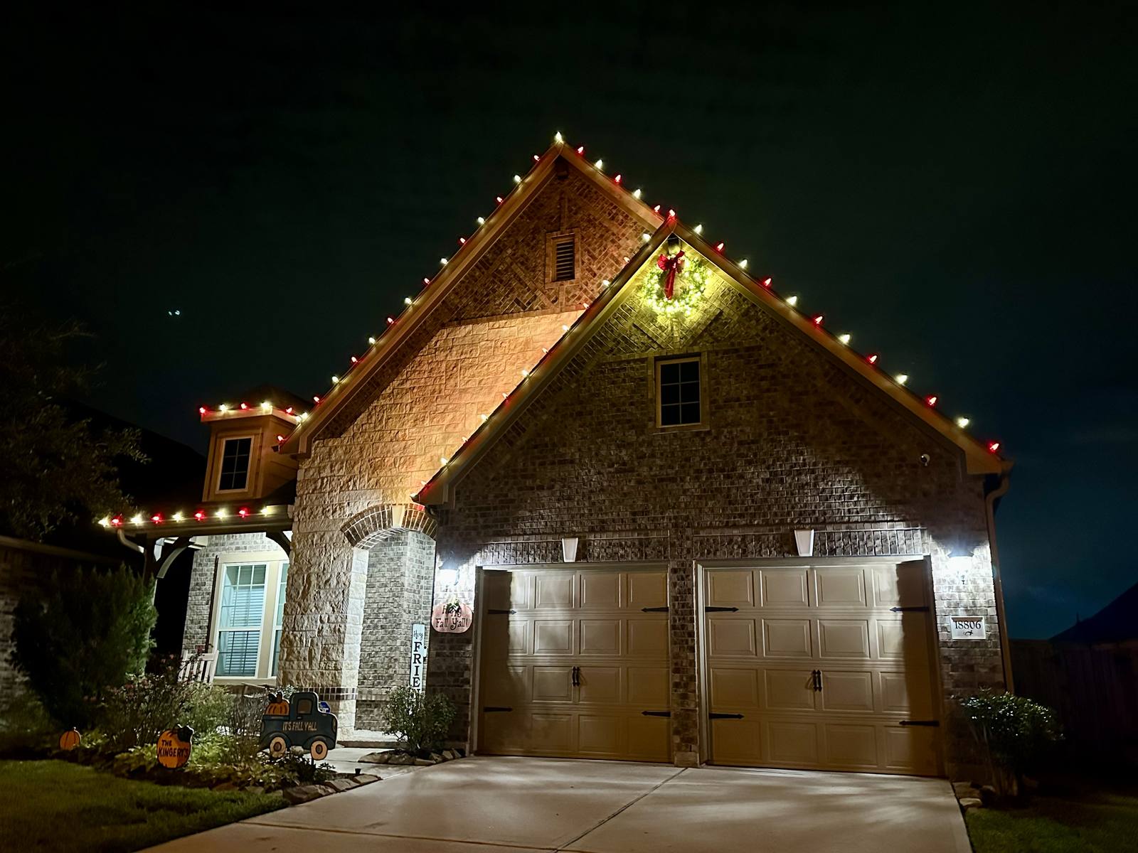Red and green C9 lights outlining a brick home's gable with a lit wreath