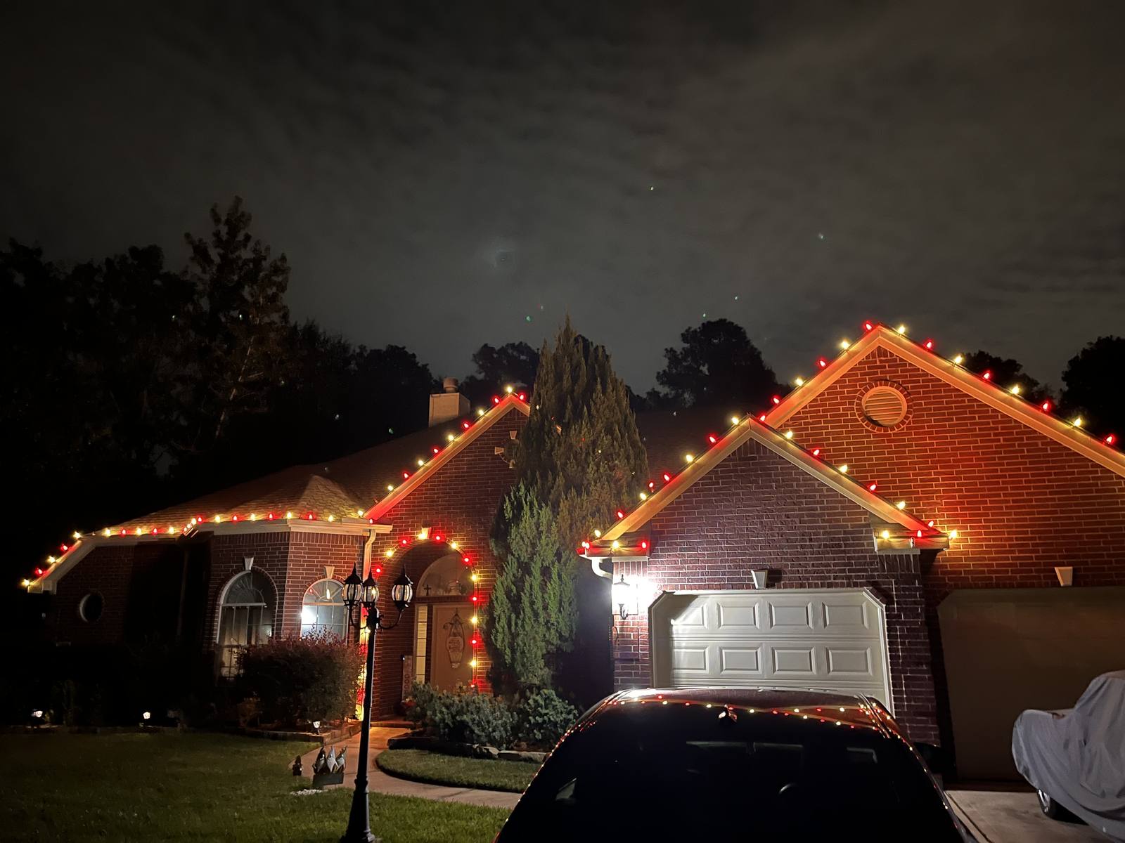 Red and white C9 roofline lighting on a brick ranch home at dusk