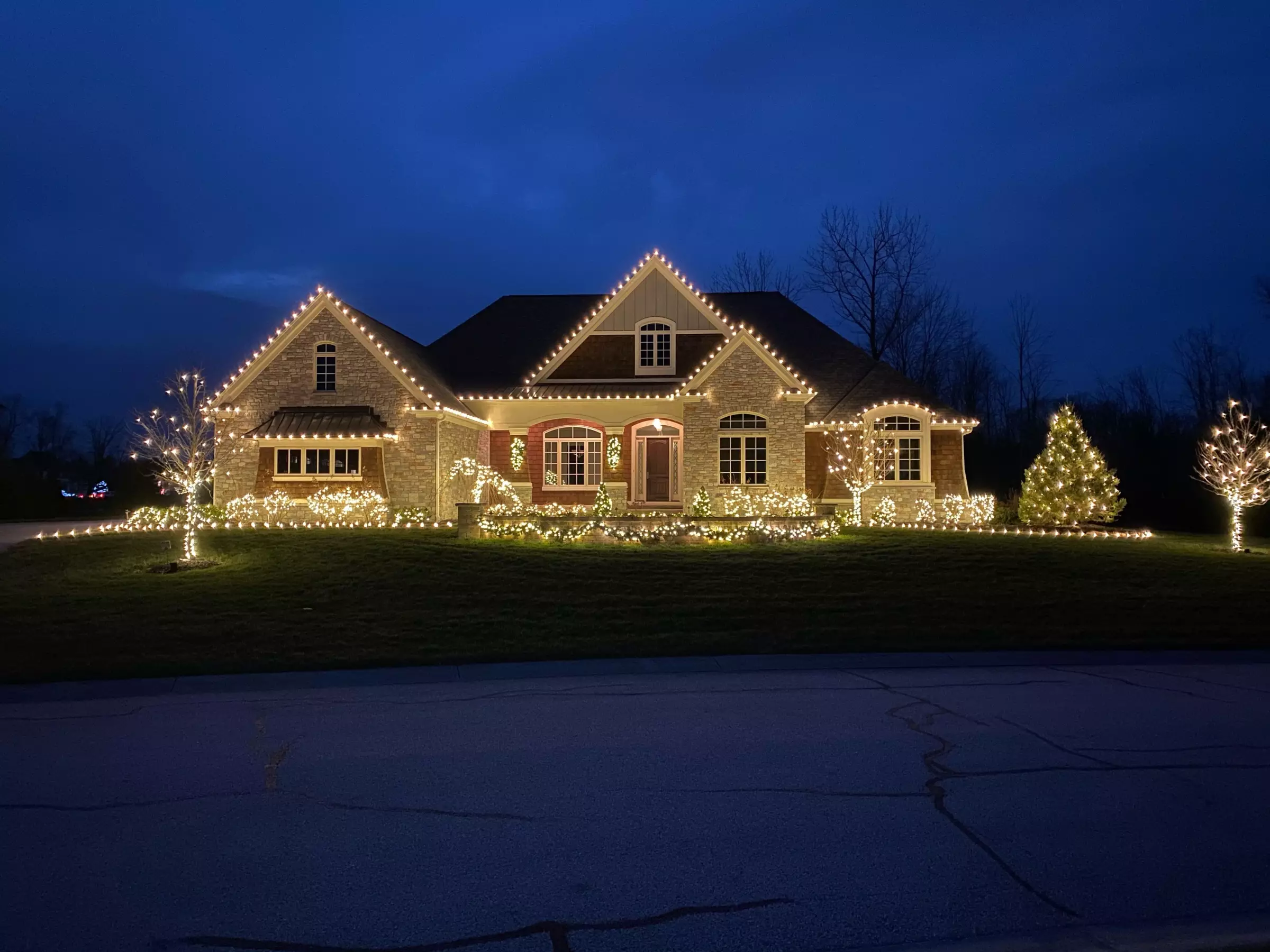 High-end Houston home with warm white Christmas roofline lighting at twilight